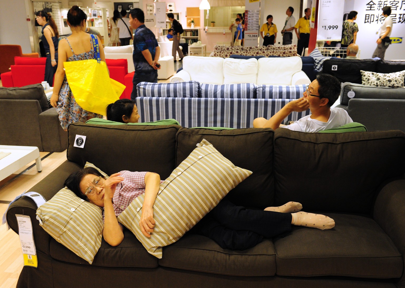 An elderly Chinese (bottom) women rests on a sofa as people shop at an Ikea frurniture store in Beijing on August 15, 2011. Asia, including China and India, will be vulnerable if the US and Europe slip into another recession, Singapore Prime Minister Lee Hsien Loong said in his annual policy speech, Lee warned it was possible the world would sink into another recession because of the debt crisis in Europe and the United States' economic woes that led to a landmark downgrade by Standard & Poor's of the country's top-notch credit ratings.  AFP PHOTO / Mark RALSTON (Photo credit should read MARK RALSTON/AFP/Getty Images)