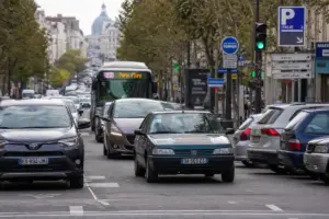 Traffico cittadino con auto moderne e vecchie, autobus in corsia e segnaletica di parcheggio e direzioni stradali