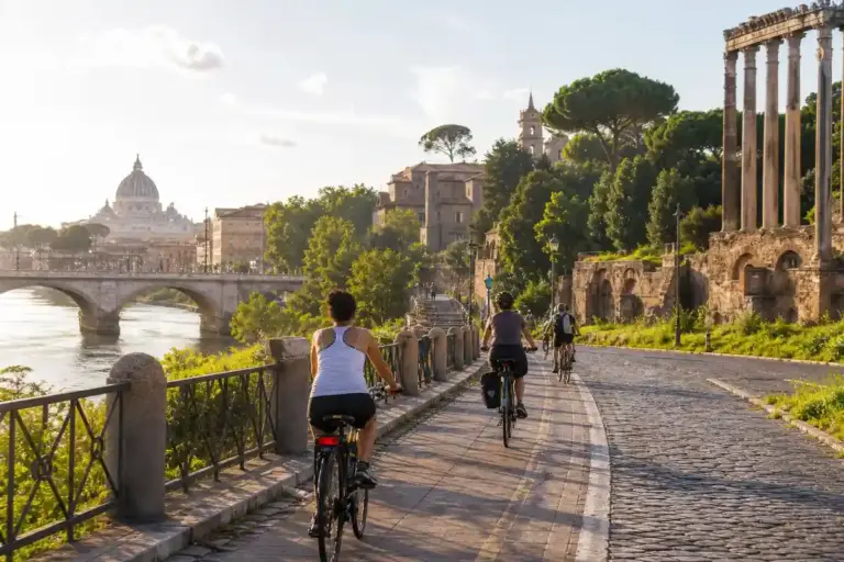 Ciclisti su una pista lungo il fiume a Roma, con ponte, Cupola di San Pietro e rovine antiche sullo sfondo