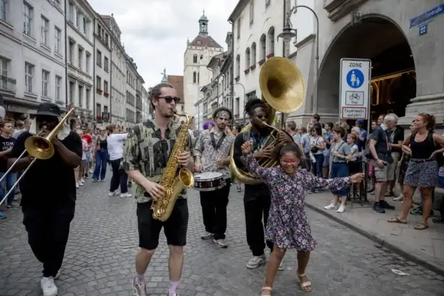 Parata di musicisti con sax, trombone, tuba e tamburo tra la folla in una strada del centro storico