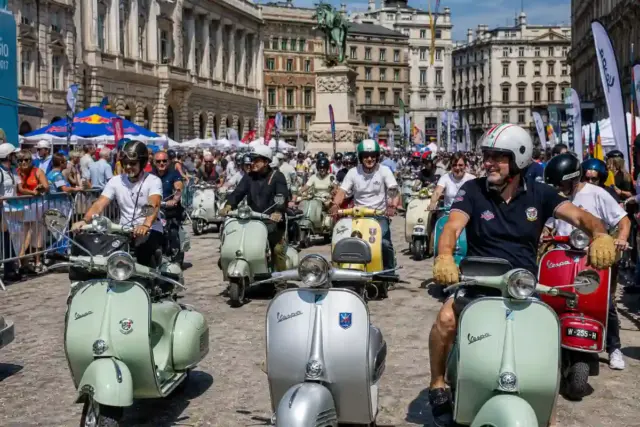 Parata di Vespa d’epoca con scooter colorati e motociclisti in una piazza affollata tra palazzi storici