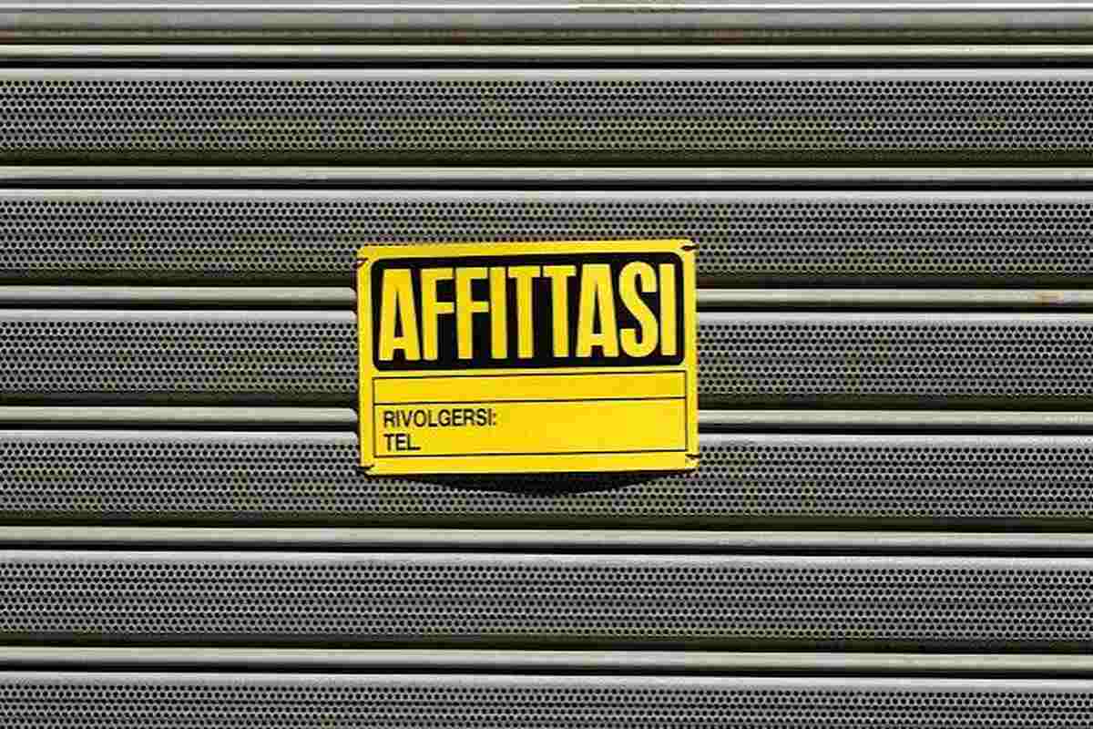 Cartello affittasi giallo su saracinesca metallica chiusa