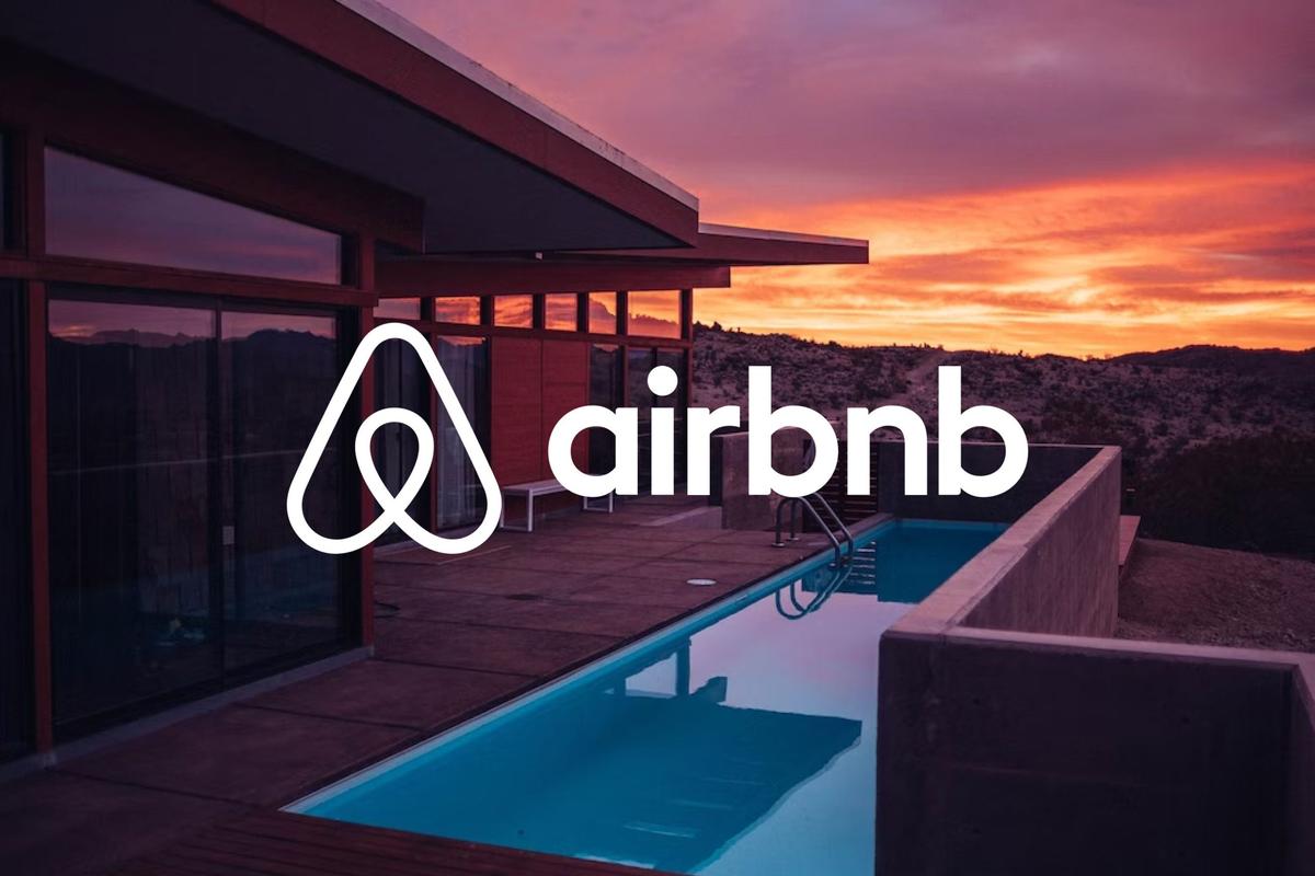 Logo Airbnb in bianco su sfondo di villa moderna con piscina al tramonto