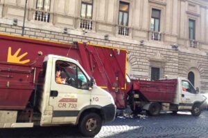 Camion AMA Roma per la raccolta rifiuti in una via del centro storico con palazzo storico sullo sfondo