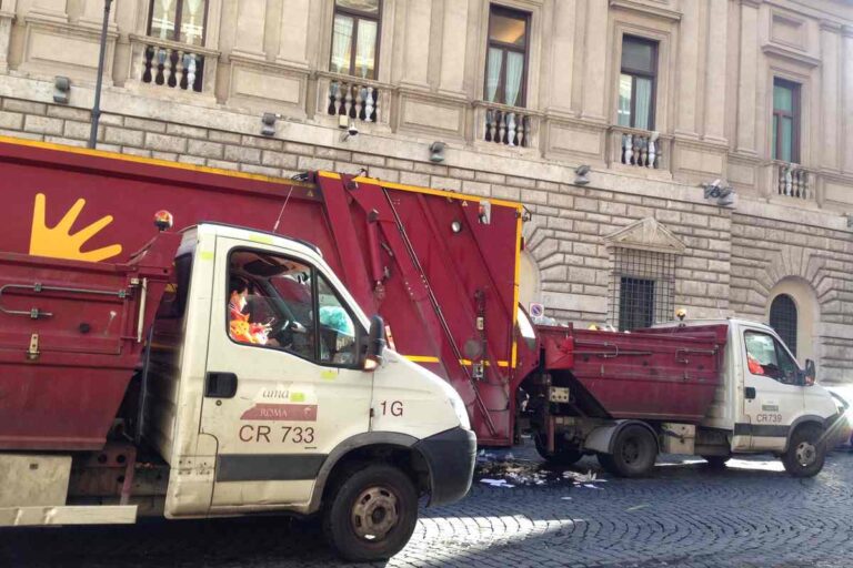 Camion AMA Roma per la raccolta rifiuti in una via del centro storico con palazzo storico sullo sfondo