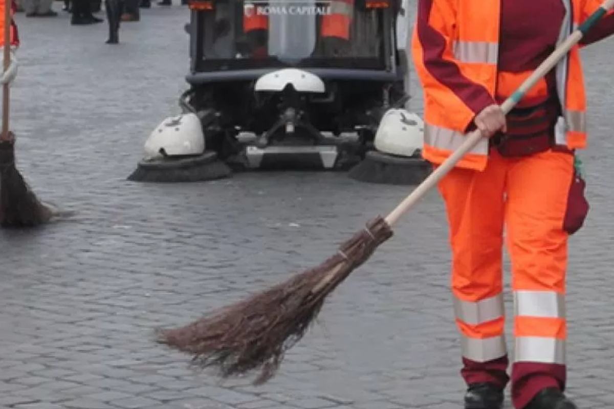 Operatori ecologici Roma Capitale spazzano una piazza con scope tradizionali davanti a uno spazzatrice meccanica