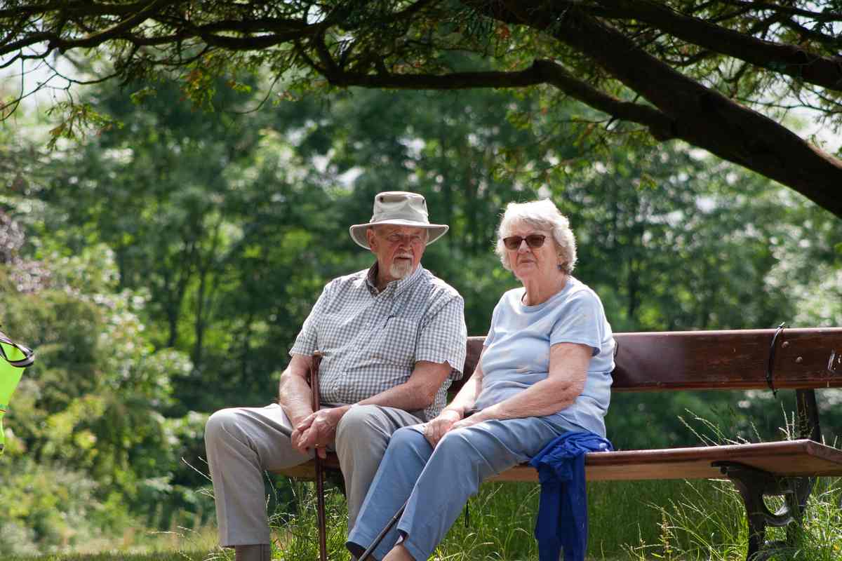 Coppia di anziani seduta su una panchina in un parco verde sotto un albero in una giornata estiva
