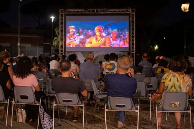 Una immagine di una arena esterna per la visione di film, con spettatori seduti di spalle.