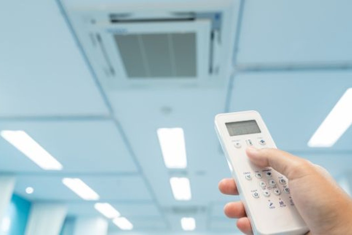 Mano che punta il telecomando verso un climatizzatore a soffitto in un ambiente luminoso