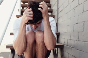 Un ragazzo seduto su una scala con le mani poggiate sulla testa
