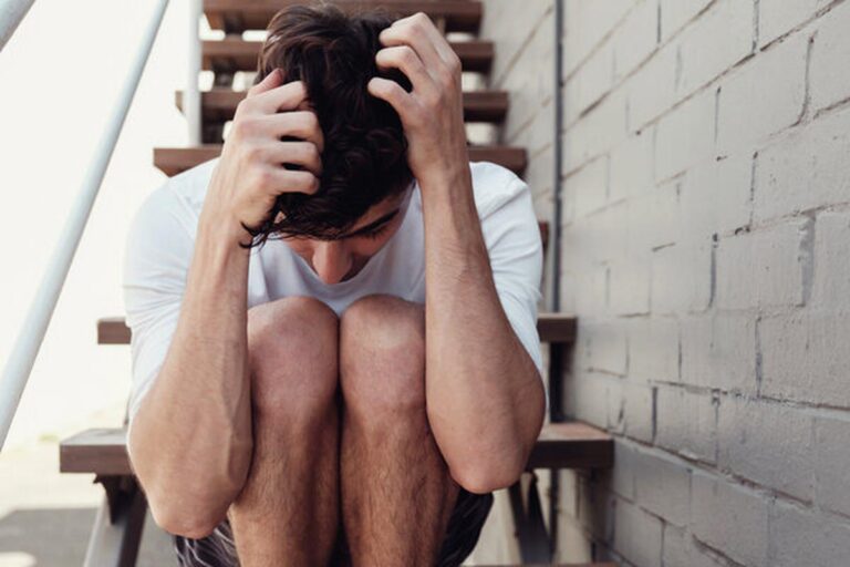 Un ragazzo seduto su una scala con le mani poggiate sulla testa