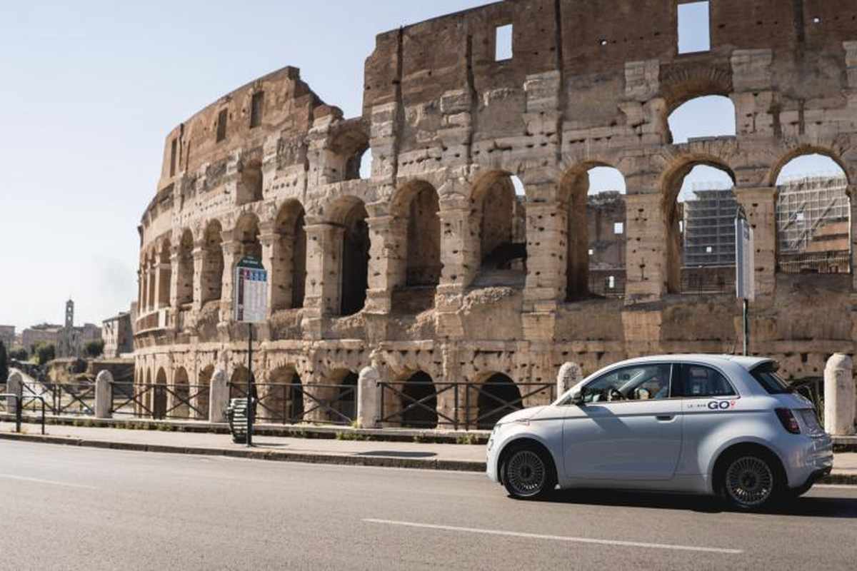 Fiat 500 elettrica bianca in sosta davanti al Colosseo di Roma in una giornata di sole