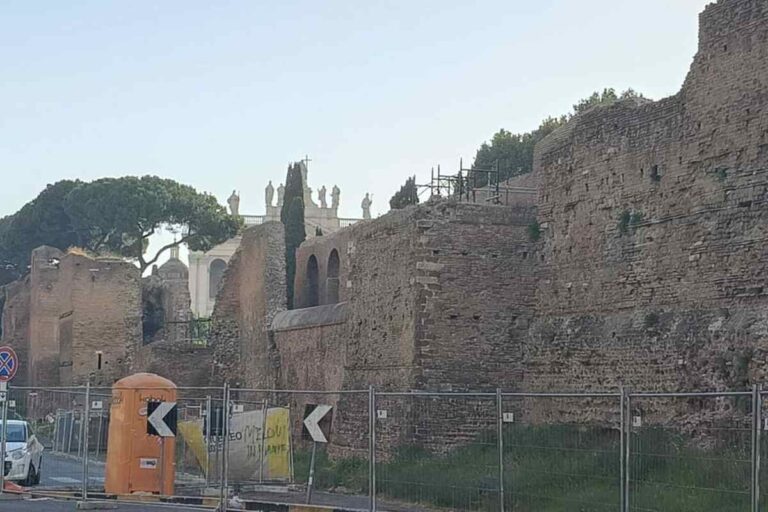 Tratto delle mura aureliane a Roma con recinzione di cantiere e vegetazione sullo sfondo