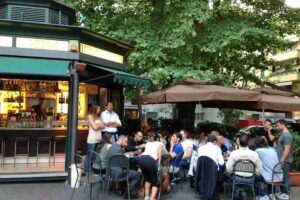 Chiosco bar all'aperto a Roma con tavolini affollati sotto gli alberi durante la sera