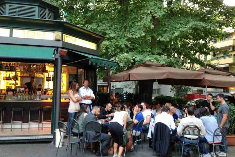 Chiosco bar all'aperto a Roma con tavolini affollati sotto gli alberi durante la sera