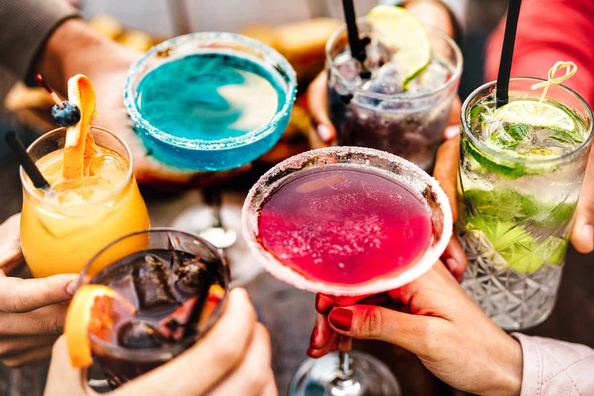 Gruppo di amici brinda con cocktail colorati durante un aperitivo
