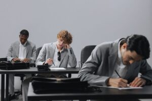 Tre candidati in giacca grigia concentrati durante le prove scritte di un concorso pubblico