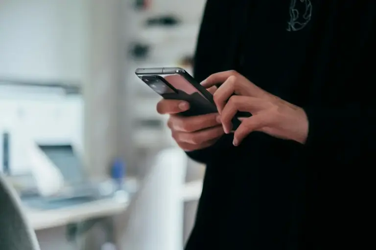 Primo piano di un uomo con in mano uno smartphone mentre visualizza il suo conto corrente online