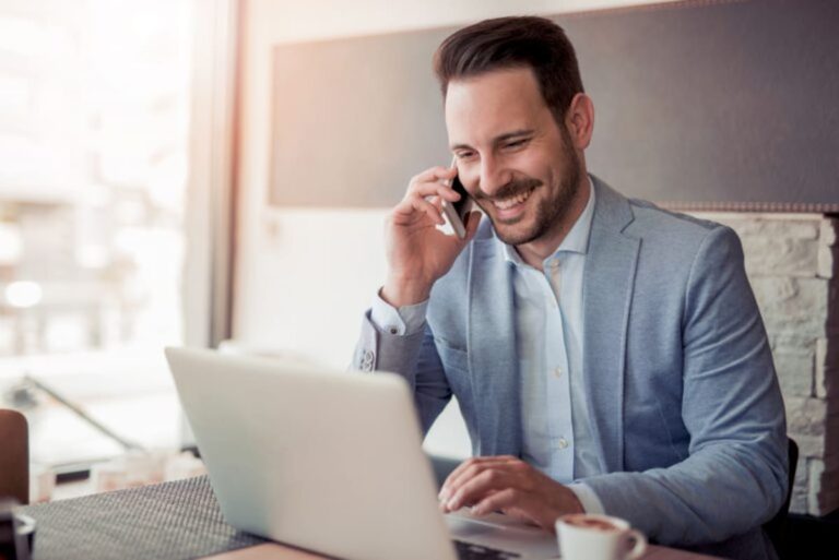 Un libero professionista alla scrivania con laptop aperto dialoga con un suo cliente al telefono