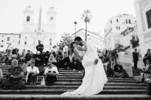 Foto in bianco e nero di un servizio fotografico di due sposi sulla gradinata di Piazza di Spagna a Roma, mentre si scambiano un abbraccio e un bacio