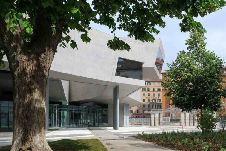 Facciata esterna del museo MAXXI di Roma progettato da Zaha Hadid, con struttura in cemento a sbalzo e alberi in primo piano