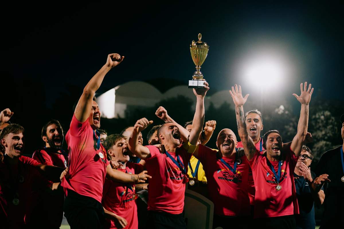 Squadra di calcio in maglia rosa esulta sollevando un trofeo dopo la vittoria notturna