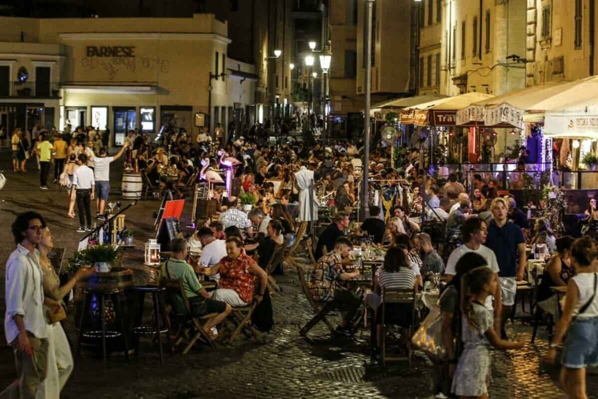 Una via di Roma di notte con locali e avventori