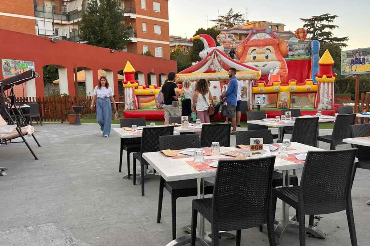 Area esterna di un locale a Roma con gonfiabili per bambini, tavoli apparecchiati e persone