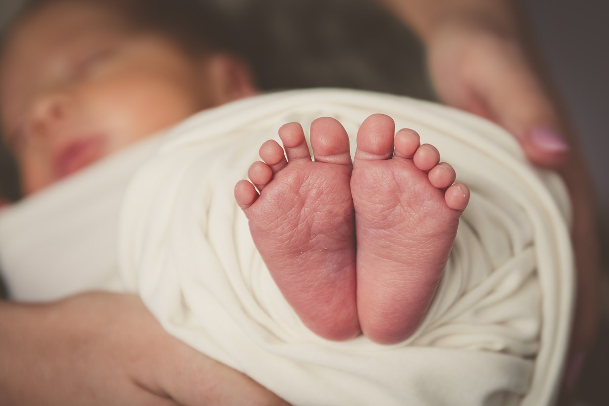 Primo piano dei piedini di un neonato avvolto in una copertina bianca, con il viso sullo sfondo sfocato