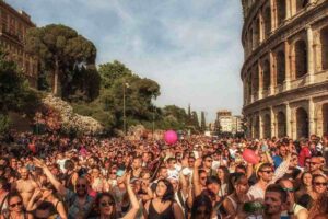 Folla del Roma Pride che sfila lungo Via Sacra con il Colosseo visibile sulla destra