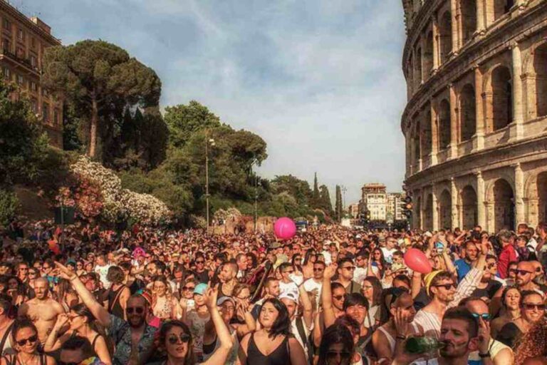 Folla del Roma Pride che sfila lungo Via Sacra con il Colosseo visibile sulla destra