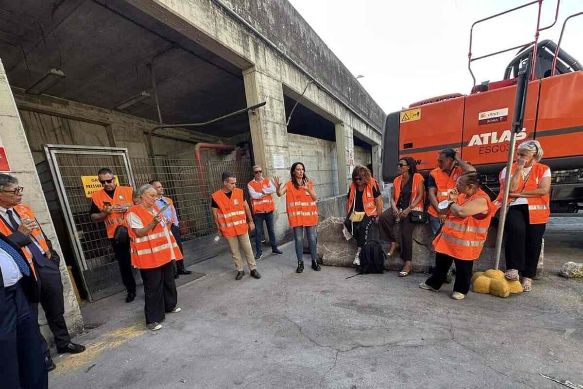 Capannone industriale dell'impianto di Rocca Cencia con operatori in gilet arancione sul piazzale