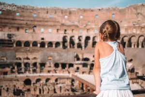 Bambina vista di spalle osserva l'interno del Colosseo di Roma in una giornata di sole