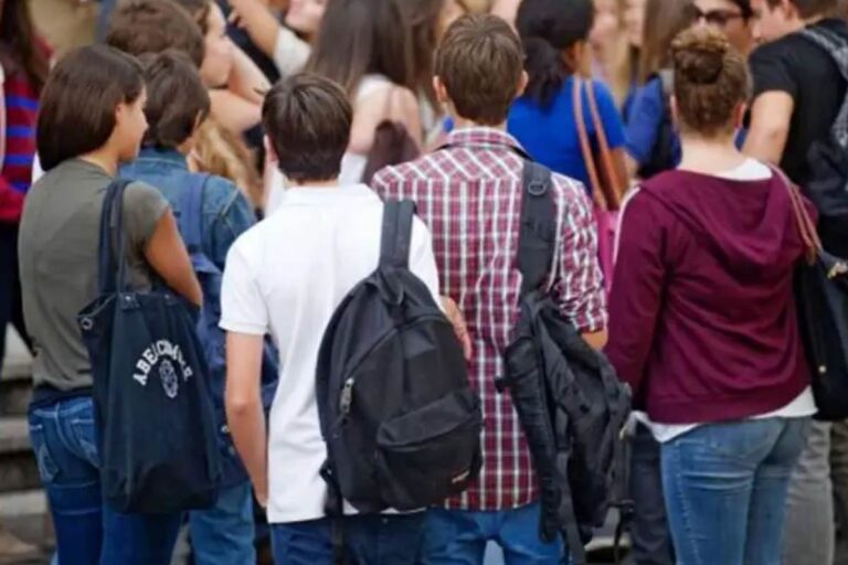 Gruppo di studenti adolescenti con zaini in spalla visti di spalle davanti a una scuola