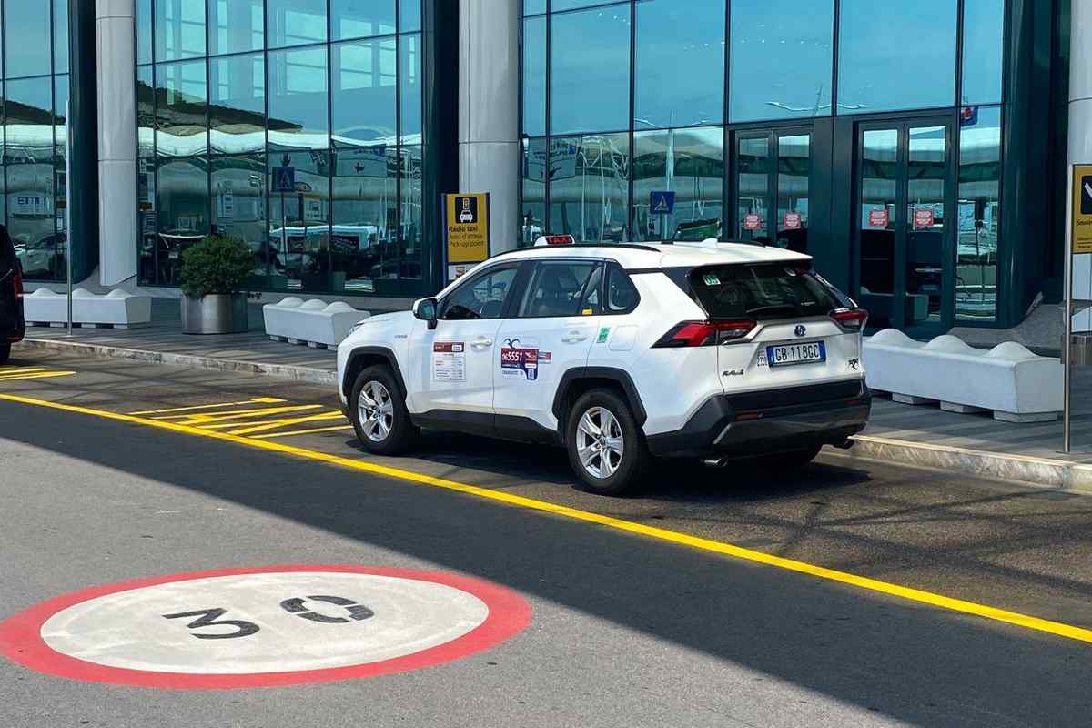 Taxi bianco Toyota RAV4 nell'area pick-up dell'aeroporto di Fiumicino, con cartello Radio Taxi sullo sfondo