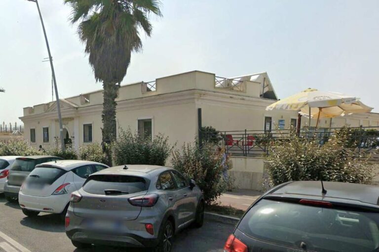 Edificio storico dello stabilimento balneare con auto parcheggiate e palme sul lungomare