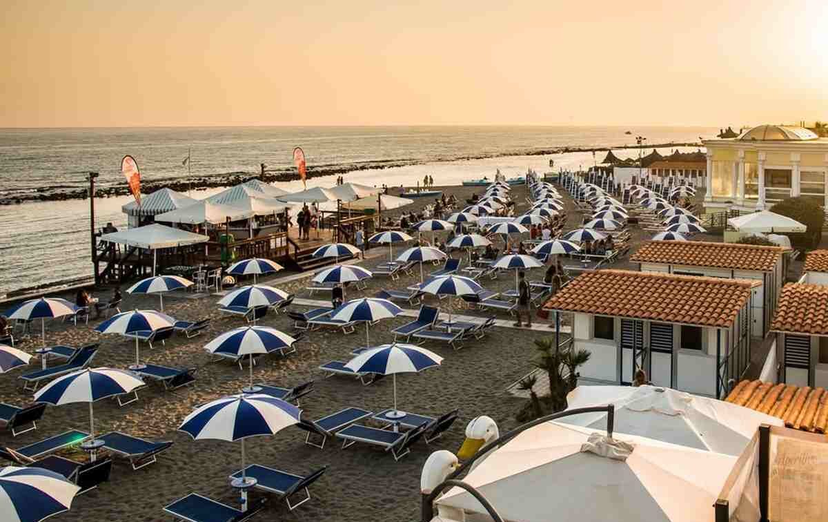 Stabilimento balneare al tramonto con file di ombrelloni bianchi e blu sulla spiaggia