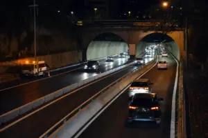 Traffico serale in ingresso e uscita da una galleria urbana a due fornici con barriere spartitraffico centrali