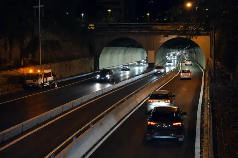 Traffico serale in ingresso e uscita da una galleria urbana a due fornici con barriere spartitraffico centrali