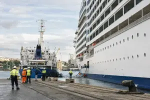 Nave da crociera affiancata a nave bunker in porto, con operatori in giubbotti alta visibilità e tubazioni di trasferimento