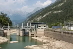 Centrale idroelettrica alpina con livello dell’acqua basso, diga in cemento e pannelli solari a lato
