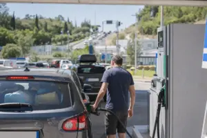 Uomo fa rifornimento a un’auto con bagagli mentre altre vetture sono in coda in un’area di servizio
