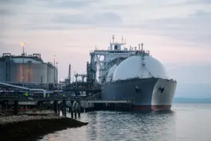 Nave metaniera GNL attraccata a un terminale con serbatoi e tubazioni, all’alba su mare calmo