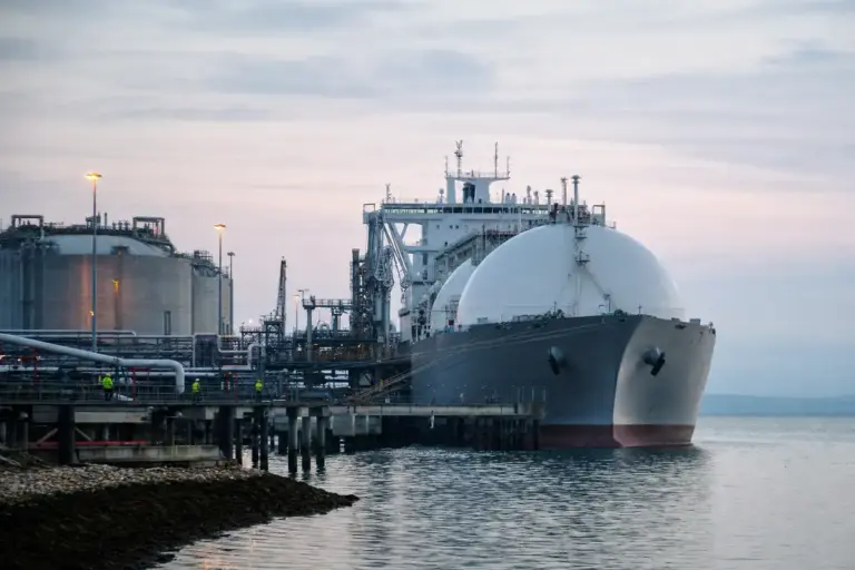 Nave metaniera GNL attraccata a un terminale con serbatoi e tubazioni, all’alba su mare calmo