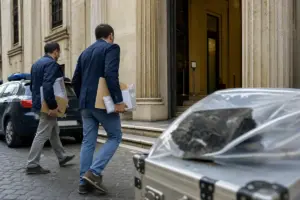 Due investigatori in abiti civili entrano in tribunale con fascicoli; in primo piano una valigetta con reperti