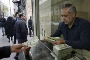 Cambiavalute dietro un vetro conta mazzette di rial mentre una mano porge banconote in dollari sulla strada