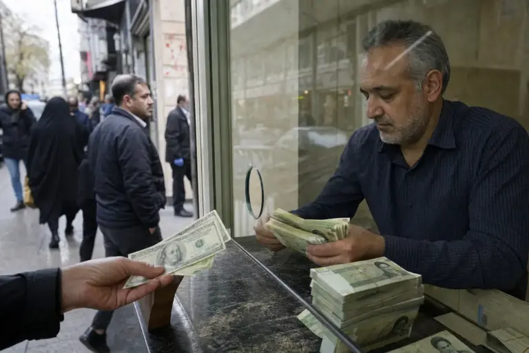Cambiavalute dietro un vetro conta mazzette di rial mentre una mano porge banconote in dollari sulla strada