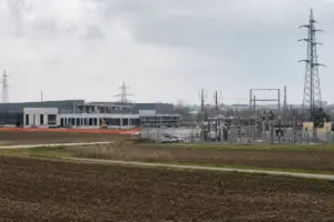 Cantiere di un edificio tipo datacenter accanto a una sottostazione elettrica e tralicci, in area agricola