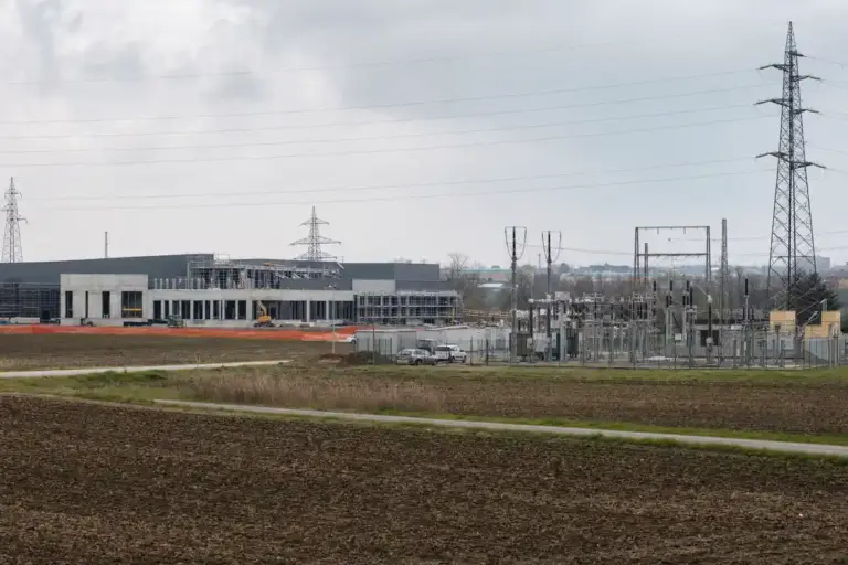 Cantiere di un edificio tipo datacenter accanto a una sottostazione elettrica e tralicci, in area agricola