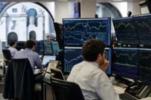 Operatore in sala trading davanti a più monitor con grafici e indici di mercato